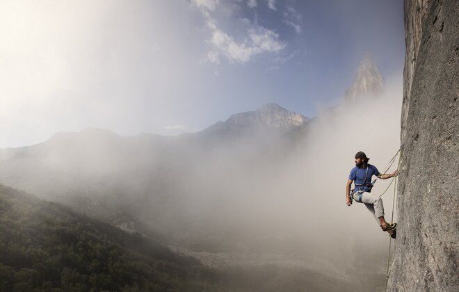Ein Männ hängt an einer Felswand im Kletterseil.
