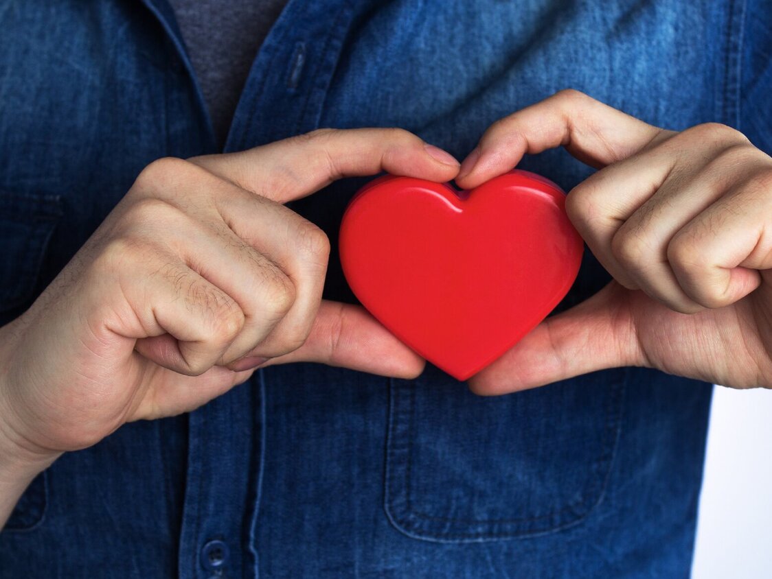 Ein Mann hält ein Holzherz direkt vor sein eigenes Herz.