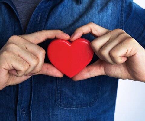 Ein Mann hält ein Holzherz direkt vor sein eigenes Herz.