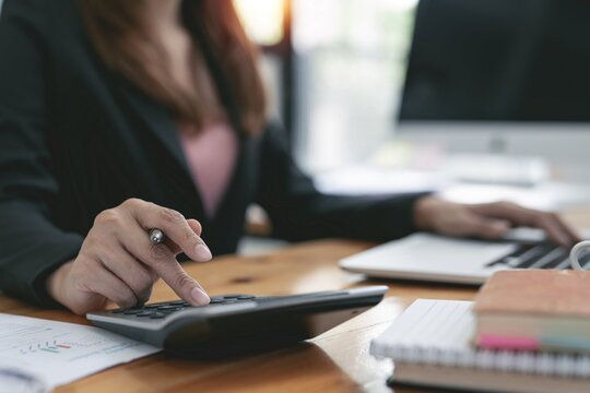 Zwei Laptops stehen auf einem Tisch. Dazwischen liegen mehrere Papiere, mit denen zwei Personen arbeiten.