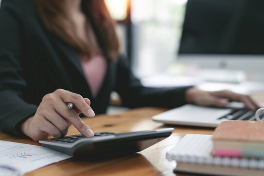 Zwei Laptops stehen auf einem Tisch. Dazwischen liegen mehrere Papiere, mit denen zwei Personen arbeiten.