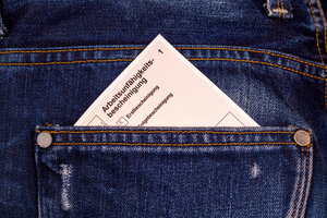 Eine Arbeitsunfähigkeitsbescheinigung steckt in der hinteren Hosentasche einer dunkelblauen Jeans.