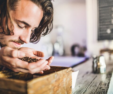 Ein Mann hält Kaffeebohnen in seiner Hand und riecht daran.