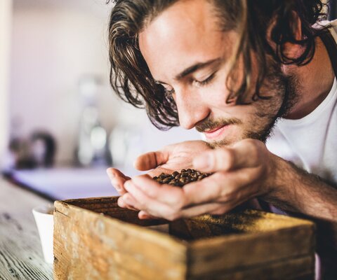Ein Mann hält Kaffeebohnen in seiner Hand und riecht daran.