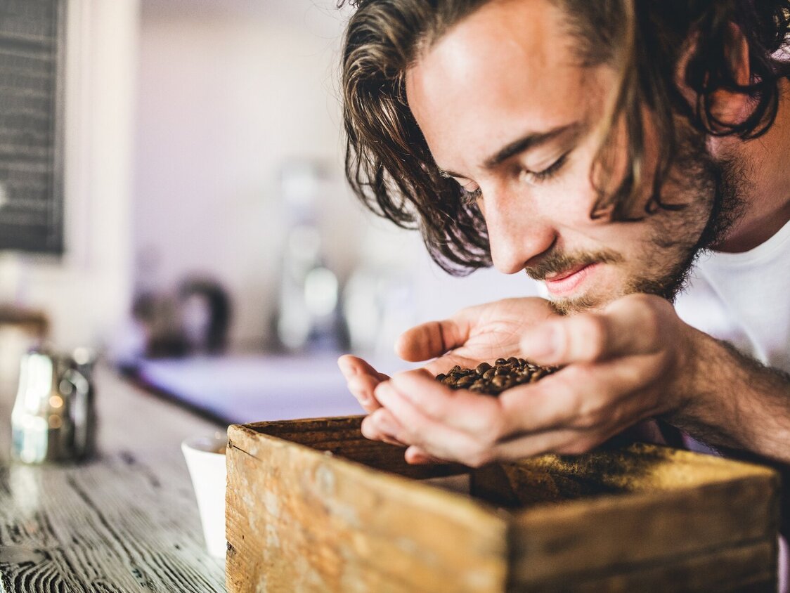 Ein Mann hält Kaffeebohnen in seiner Hand und riecht daran.