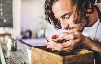 Ein Mann hält Kaffeebohnen in seiner Hand und riecht daran.