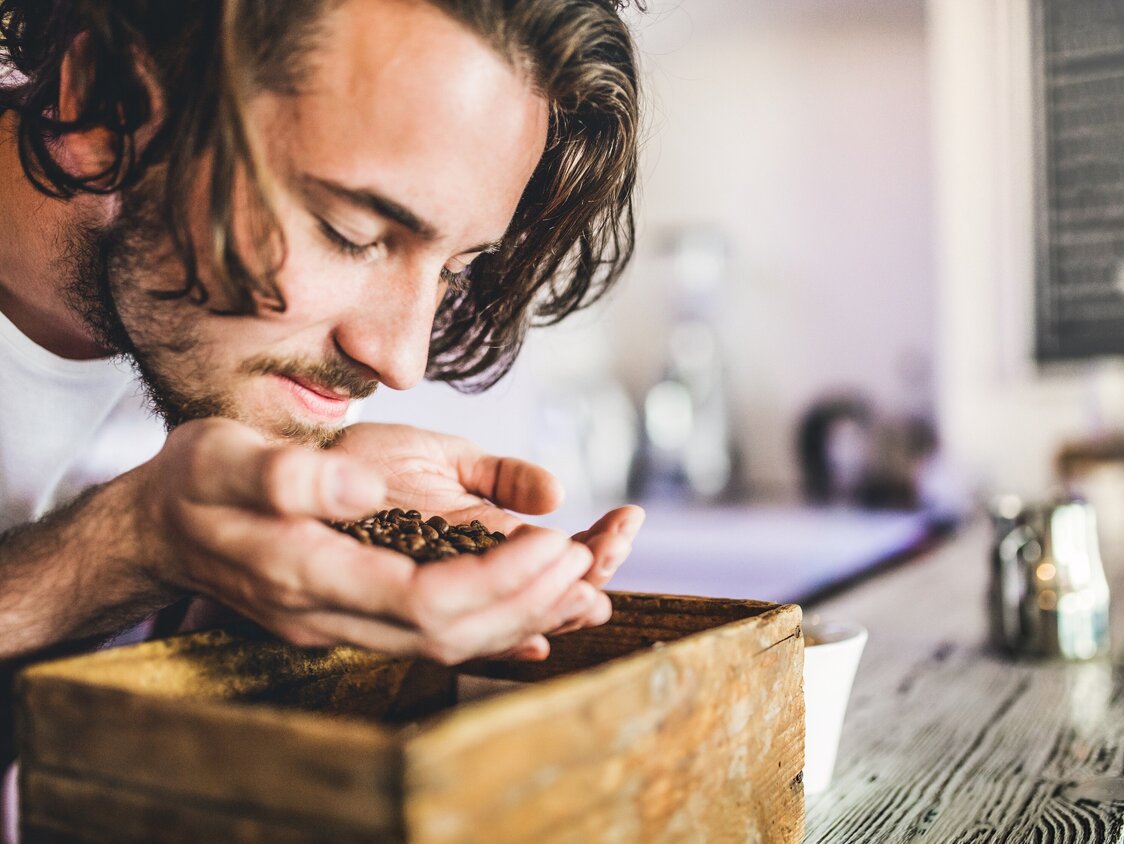 Ein Mann hält Kaffeebohnen in seiner Hand und riecht daran.