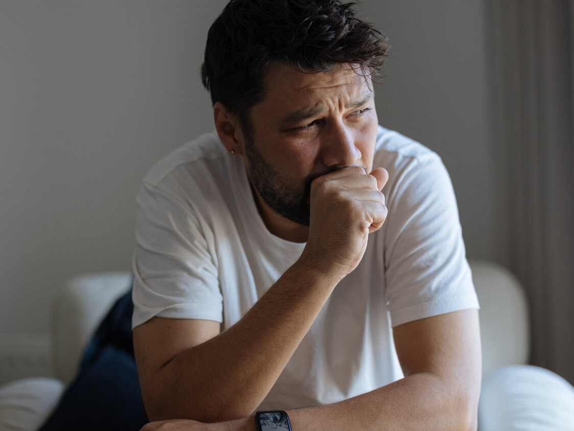 Junger Mann sitzend und hält seine Hand vor dem Mund zum husten.