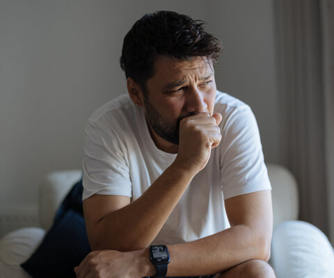 Junger Mann sitzend und hält seine Hand vor dem Mund zum husten.