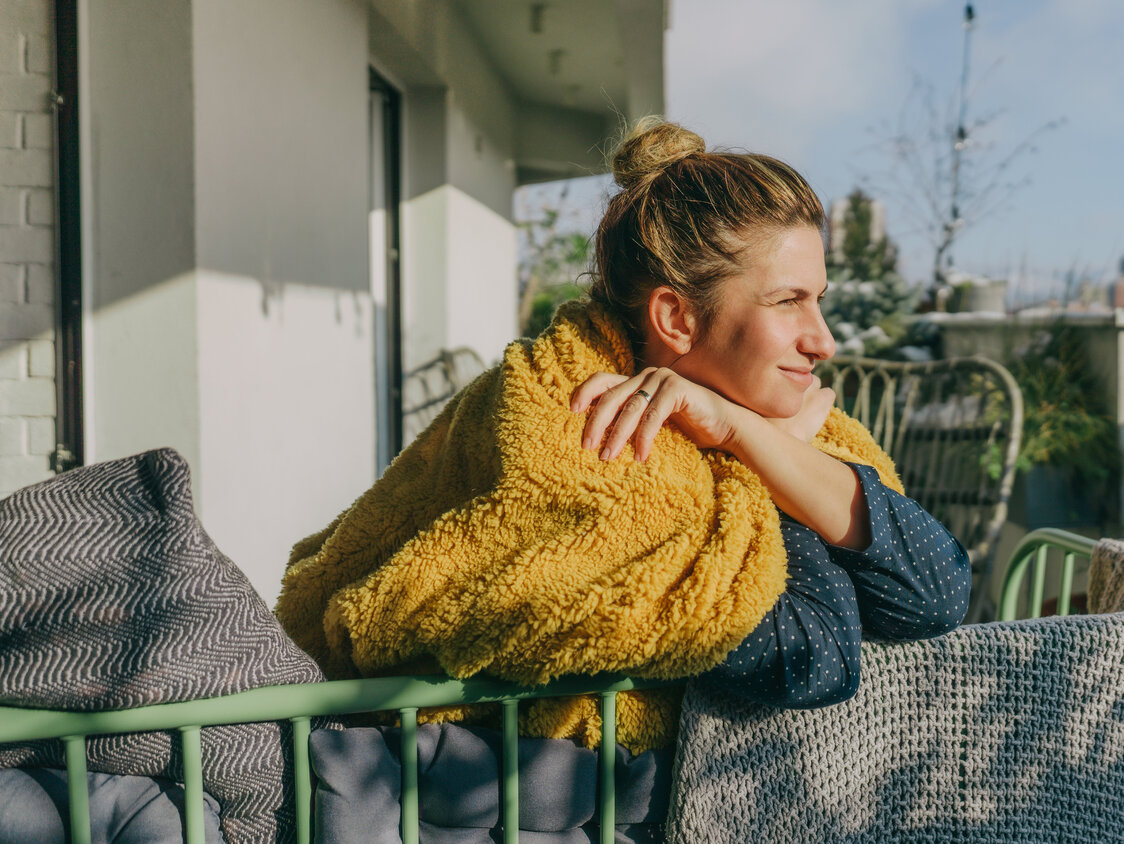 Eine Frau lehnt gegen ein Balkongeländer und hält ihr Gesicht in die Sonne.