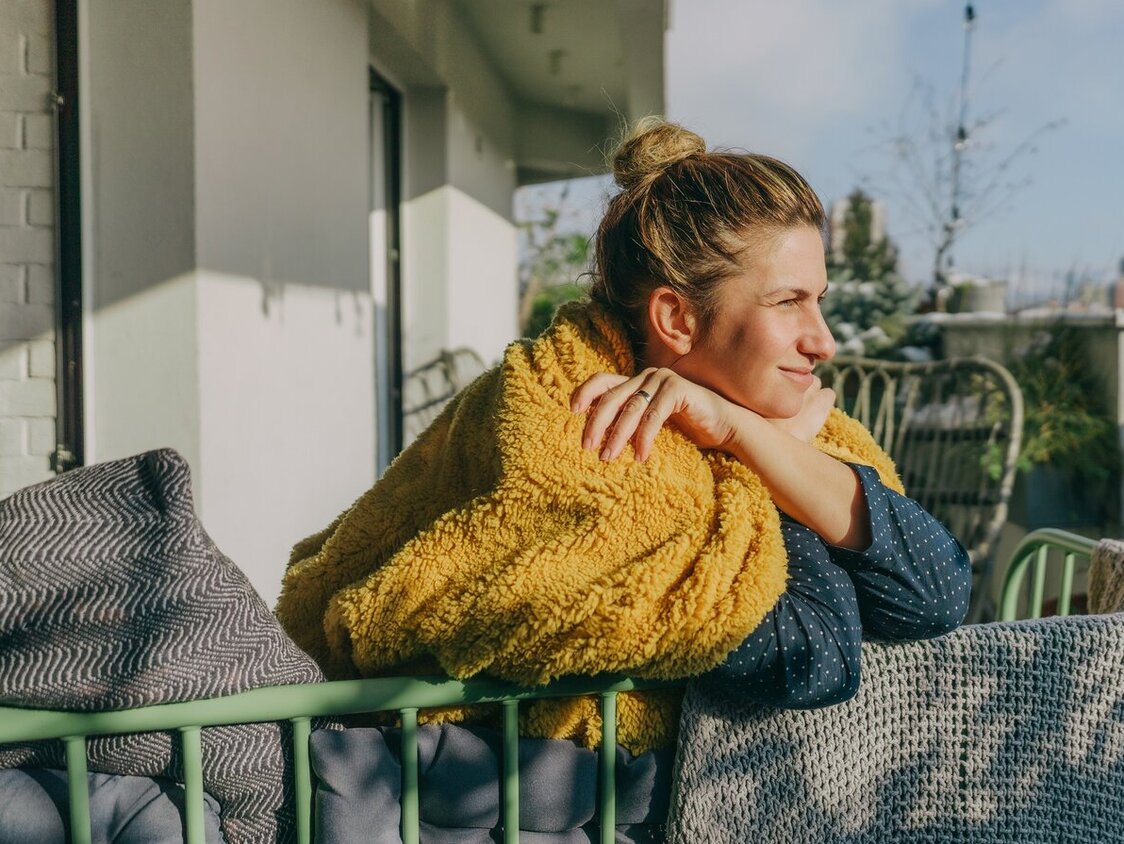 Eine Frau lehnt gegen ein Balkongeländer und hält ihr Gesicht in die Sonne.