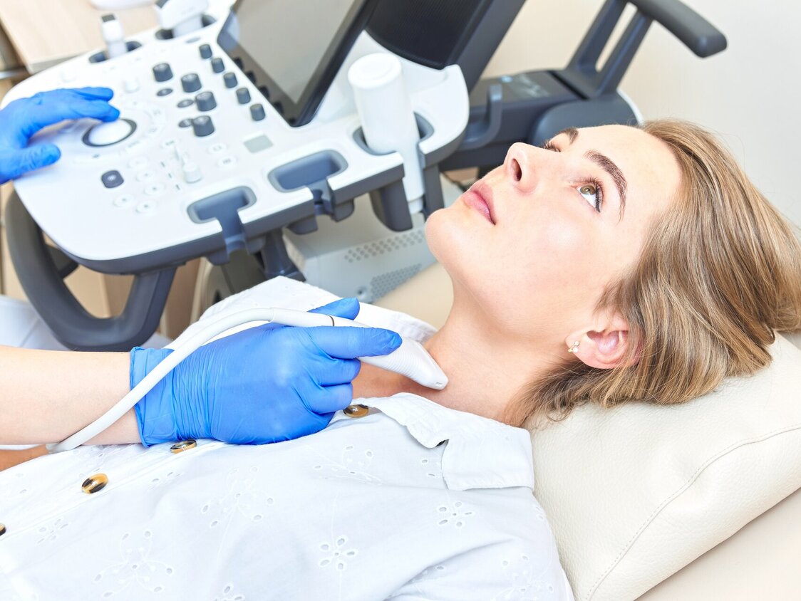 Eine Frau liegt auf einer Behandlungsliege und ihr Hals wird einem Ultraschall unterzogen.