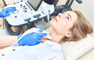 Eine Frau liegt auf einer Behandlungsliege und ihr Hals wird einem Ultraschall unterzogen.
