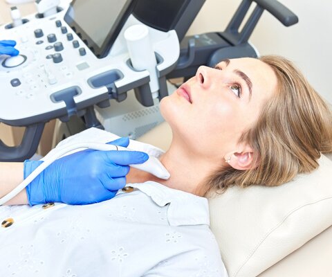 Eine Frau liegt auf einer Behandlungsliege und ihr Hals wird einem Ultraschall unterzogen.