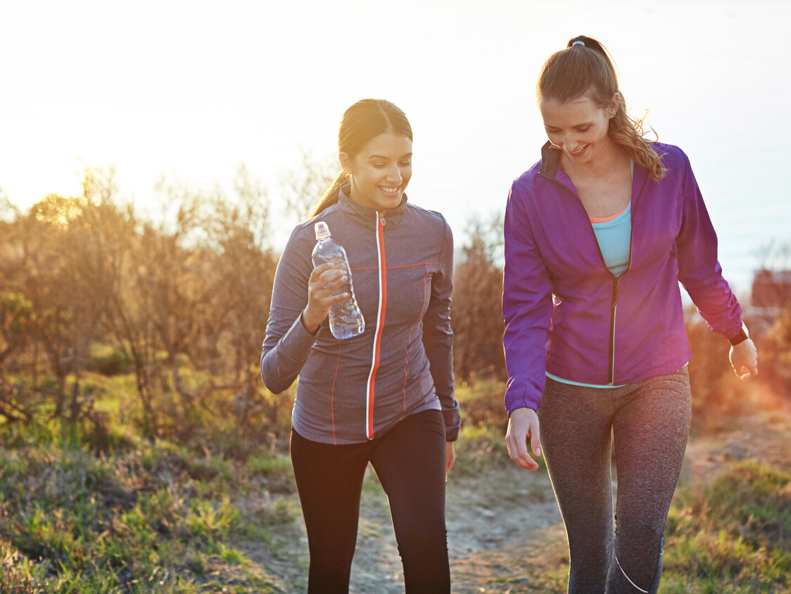 Zwei Frauen joggen durch eine herbstliche Landschaft.