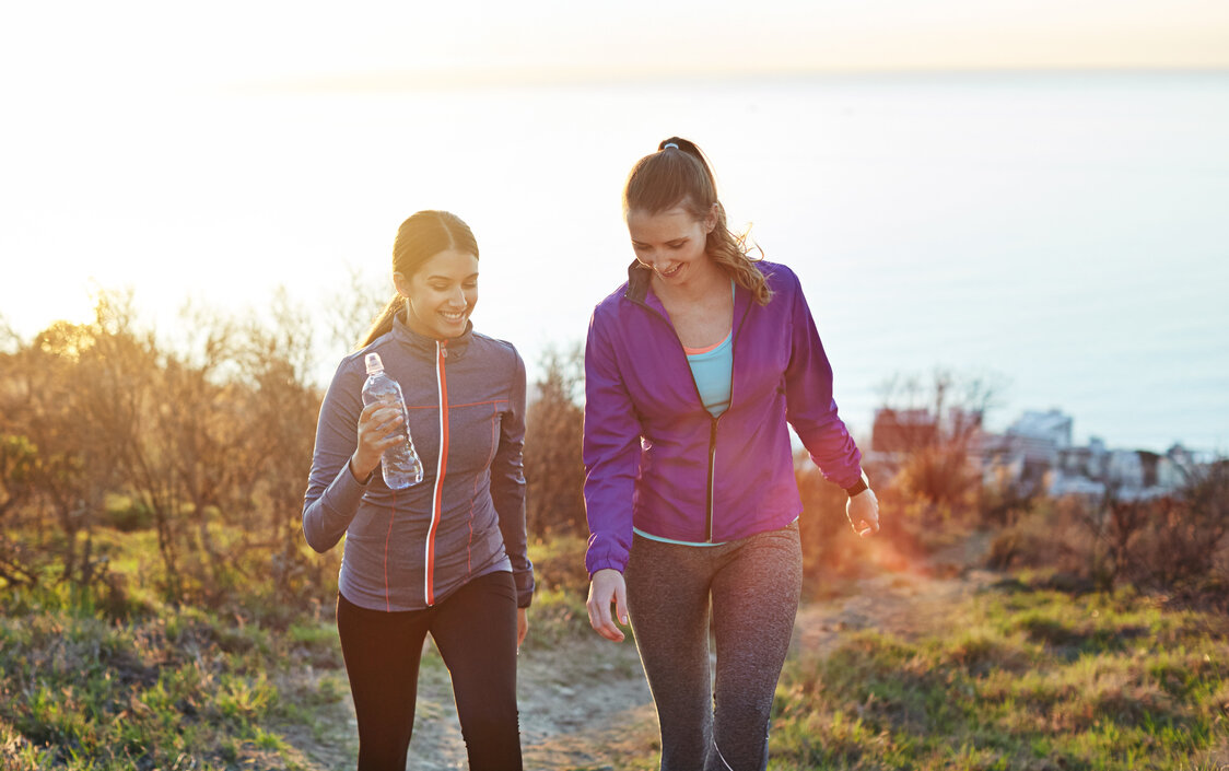 Zwei Frauen joggen durch eine herbstliche Landschaft.