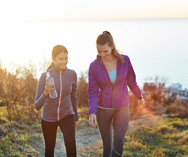 Zwei Frauen joggen durch eine herbstliche Landschaft.