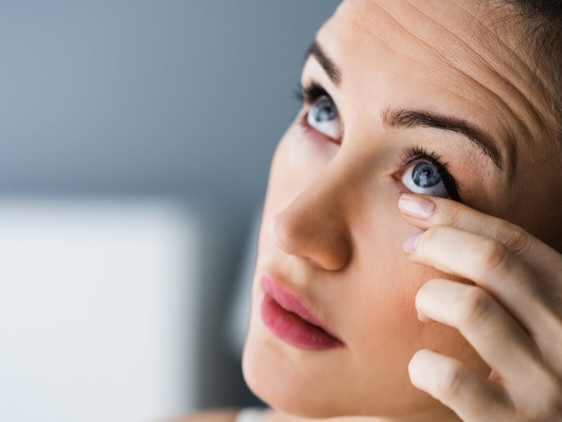 Frau fasst sich ins Auge und schaut nach oben