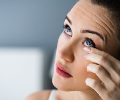 Frau fasst sich ins Auge und schaut nach oben