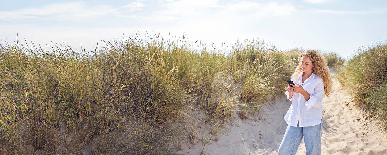 Eine Frau steht in einer Düne und guckt auf ihr Handy.