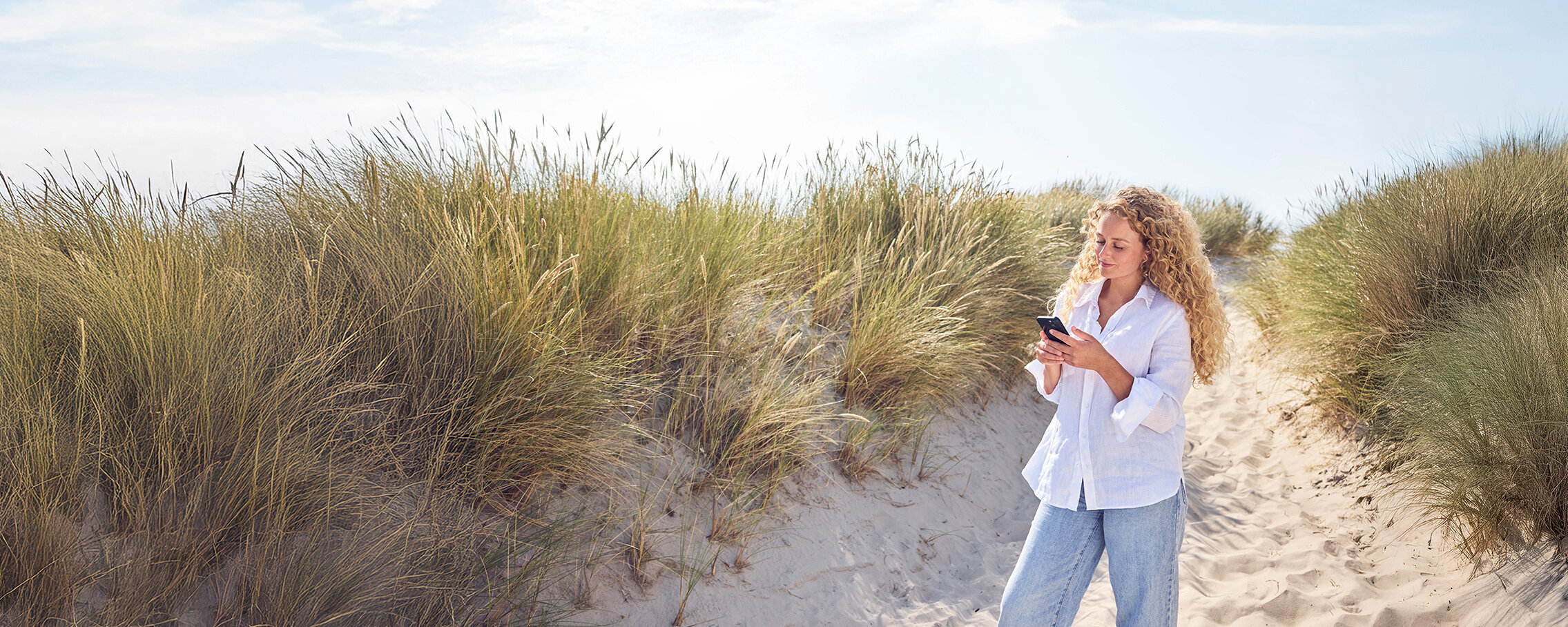 Eine Frau steht in einer Düne und guckt auf ihr Handy.