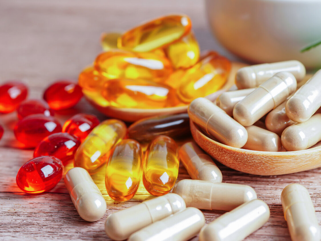 Einige verschiedenfarbige Nahrungsergänzungsmittel als Kapseln auf einem hölzernen Hintergrund. 