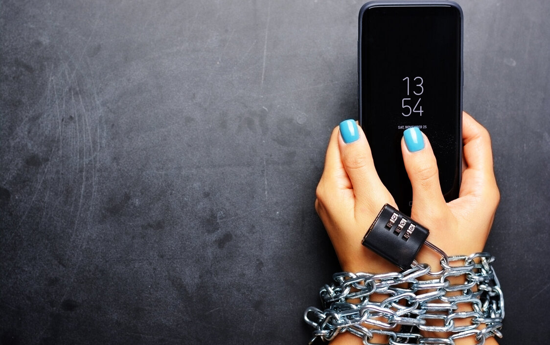 Zwei Hände die ein Smartphone halten und mit Stahlketten und einem Schloss gefesselt sind.
