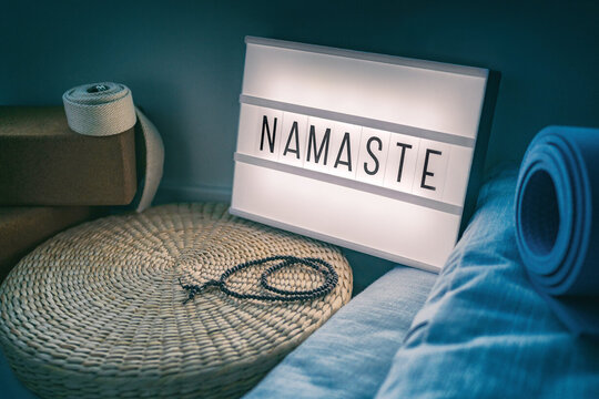 Blaue Yogamatte sowie weiteres Zubehör liegen vor einem beleuchteten Schild mit der Aufschrift "Namaste".