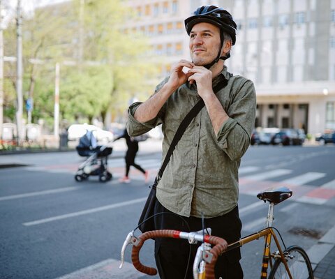 Mann mittleren Alters, der sich für das Fahrradfahren seinen Fahrradhelm festmacht.