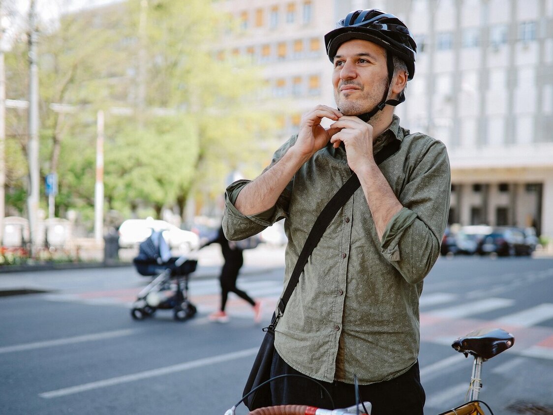 Mann mittleren Alters, der sich für das Fahrradfahren seinen Fahrradhelm festmacht.