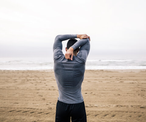 Ein Mann steht am Strand und dehnt seinen Arm.