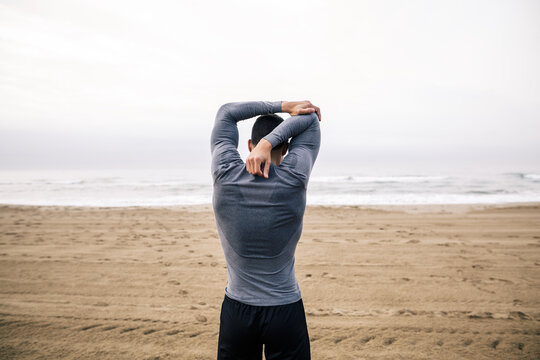 Ein Mann steht am Strand und dehnt seinen Arm.