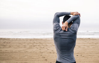 Ein Mann steht am Strand und dehnt seinen Arm.