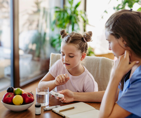 Mother checking girl's blood glucose level using a fingerstick glucose meter before meal.