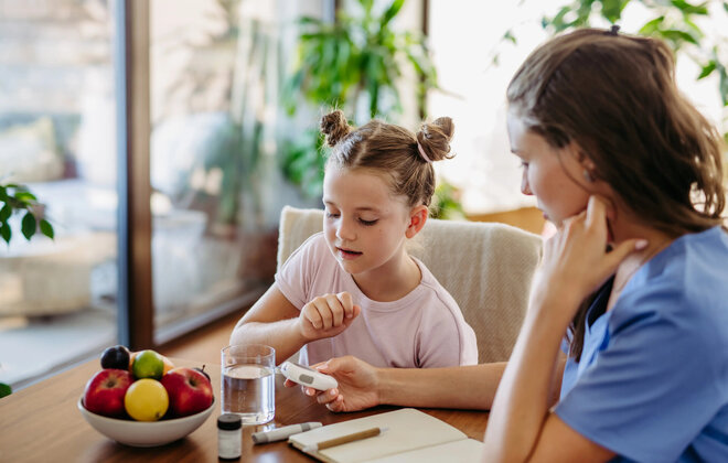 Mother checking girl's blood glucose level using a fingerstick glucose meter before meal.
