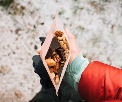 Eine Hand hält eine offene Tüte mit Nüssen und Schokolade.