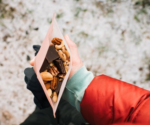 Eine Hand hält eine offene Tüte mit Nüssen und Schokolade.