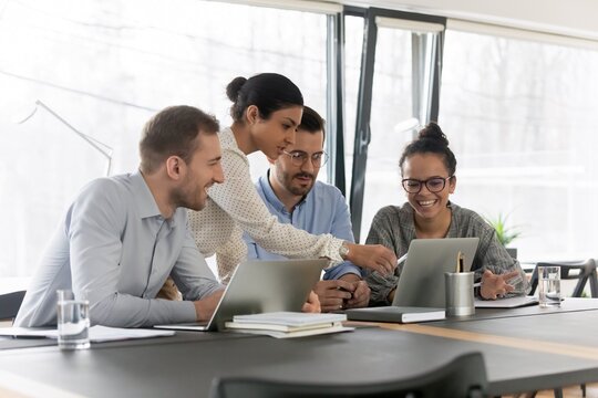 Vier Personen sitzen bzw. stehen an einem Tisch und schauen auf Laptops.