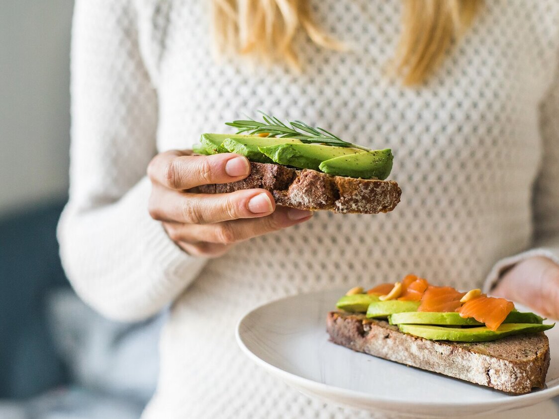 Nahaufnahme der Frau hält Platte mit Avocado-Toast als frischen Snack