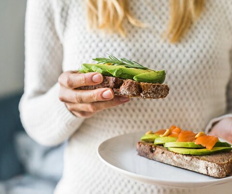 Nahaufnahme der Frau hält Platte mit Avocado-Toast als frischen Snack