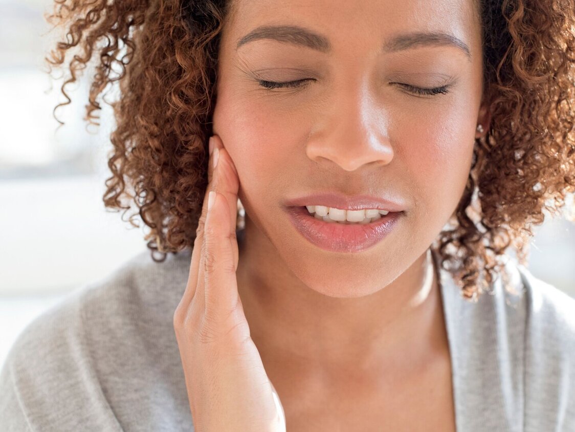 Frau greift sich an die Wange, während Sie ihr Gesicht leicht schmerzhaft verzieht.