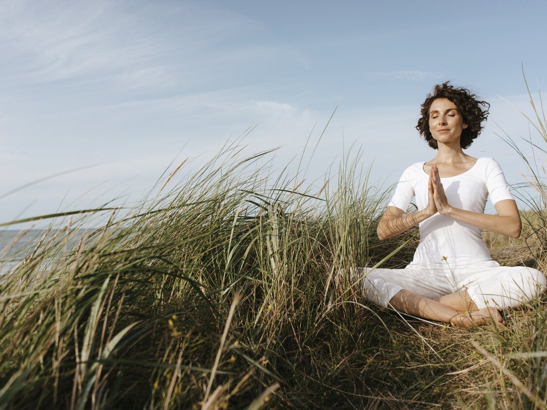 Ein Frau meditiert in den Dünen am Strand.