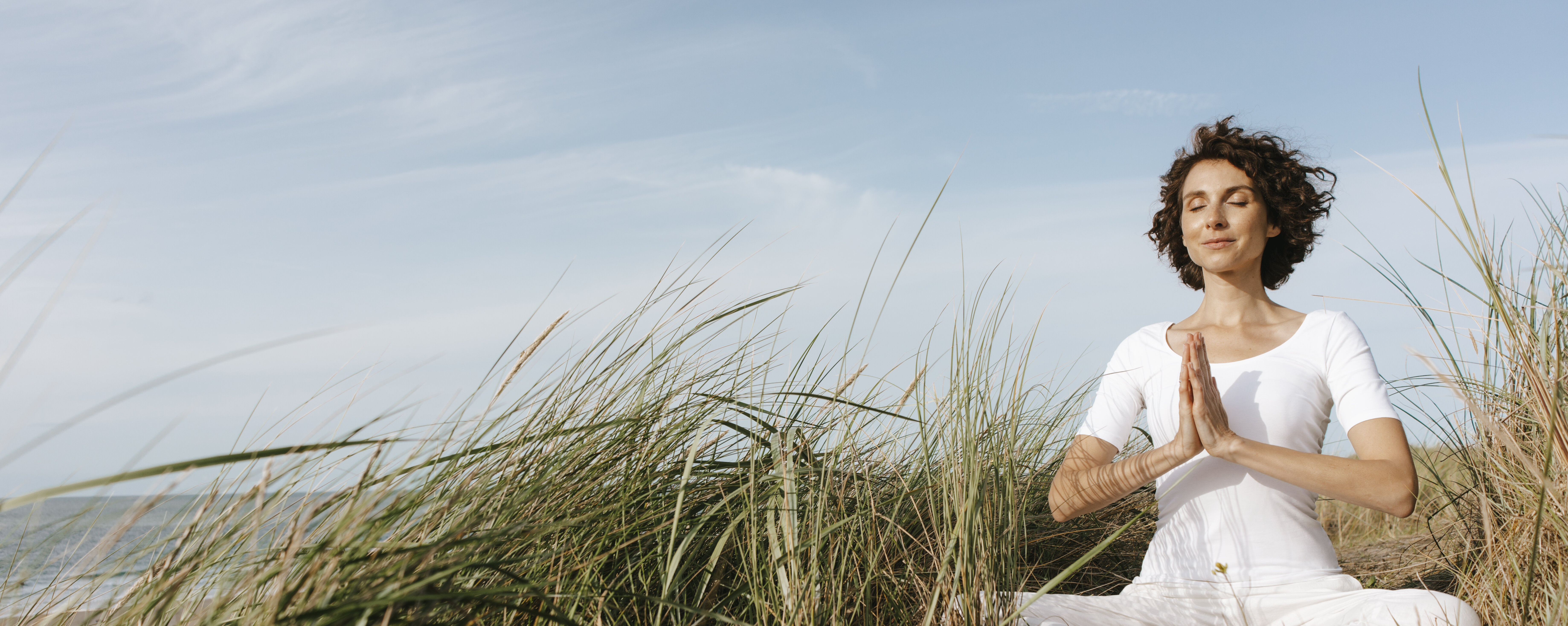 Ein Frau meditiert in den Dünen am Strand.