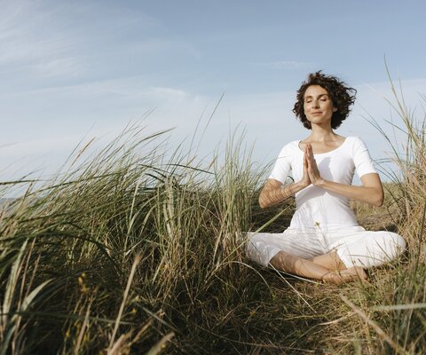 Ein Frau meditiert in den Dünen am Strand.