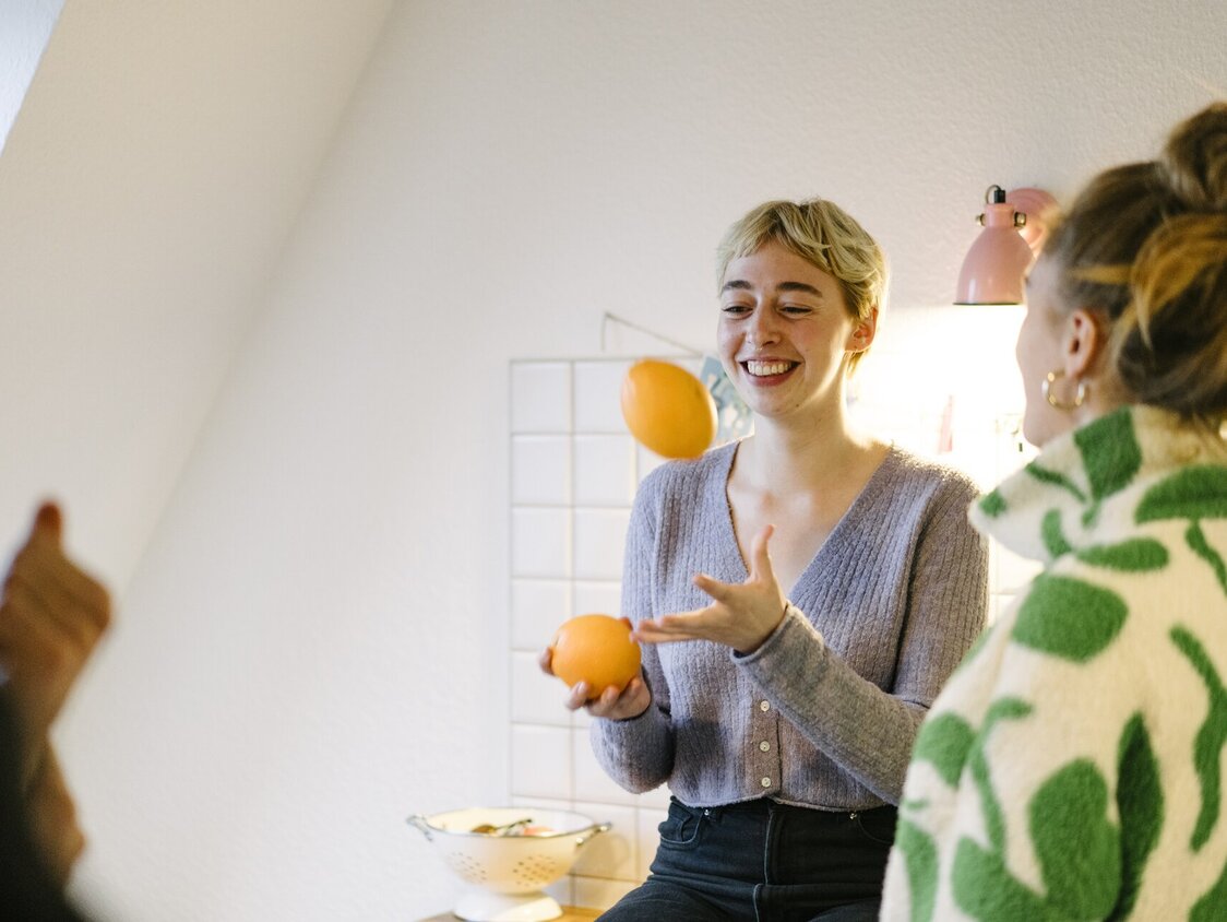 Zwei Frauen stehen in einer Küche und die eine jongliert mit zwei Orangen