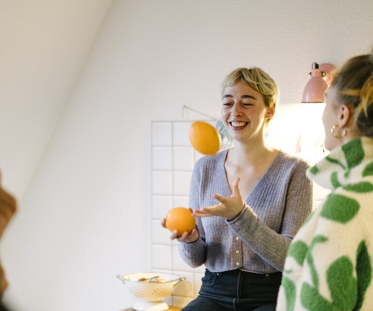 Zwei Frauen stehen in einer Küche und die eine jongliert mit zwei Orangen