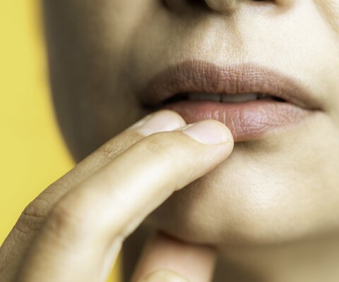 Nahaufnahme einer Frau, die sich mit zwei Finger an die Lippen fasst.