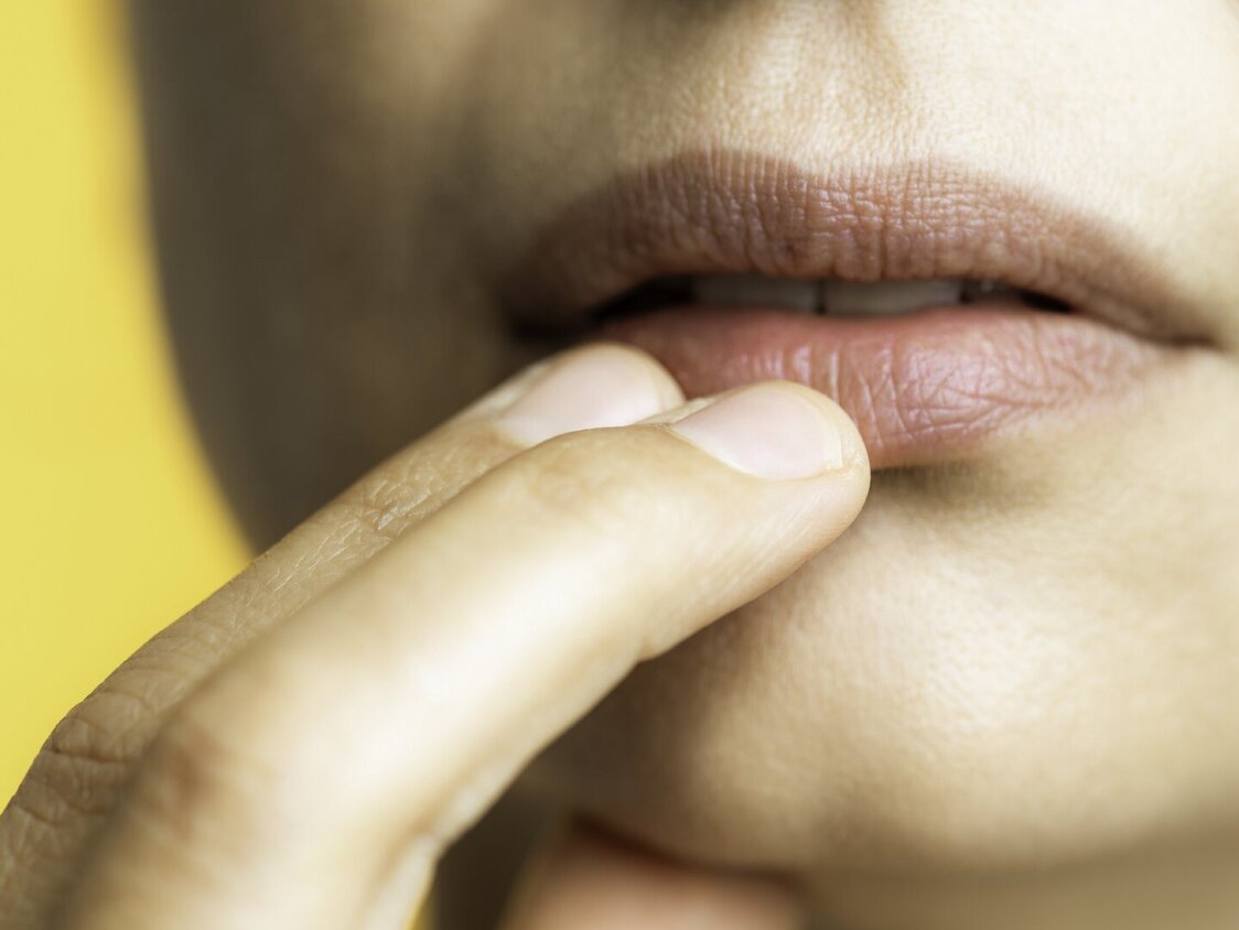 Nahaufnahme einer Frau, die sich mit zwei Finger an die Lippen fasst.