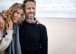 Lachendes Paar steht Arm in Arm am Strand.