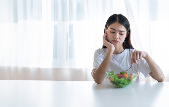 Eine Frau sitzt unglücklich vor einer Schüssel mit Salat.